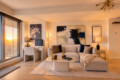 Modern living room bathed in warm sunset light with a beige sectional, abstract art, and a marble coffee table on a pale rug.