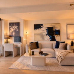 Modern living room bathed in warm sunset light with a beige sectional, abstract art, and a marble coffee table on a pale rug.