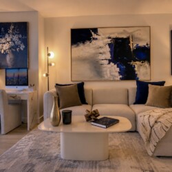 Cozy modern living room with a beige sectional, blue and brown pillows, and a cream throw on a plush rug, centered around a white oval coffee table with decorative items.