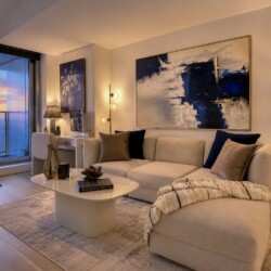 Cozy modern living room with a beige sectional, abstract blue painting, and a sunset city view through large windows.