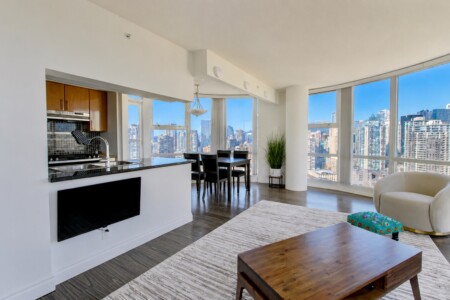 Open-concept living area with a kitchen on the left, dining table near large windows, and a city skyline view.
