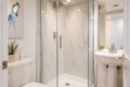 Modern bathroom with a glass-enclosed shower, marble walls, a white toilet, and a pedestal sink with a small plant on the tank area.