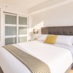 Bright hotel bedroom with a large gray upholstered bed, white linens, and a yellow accent pillow.1823757?