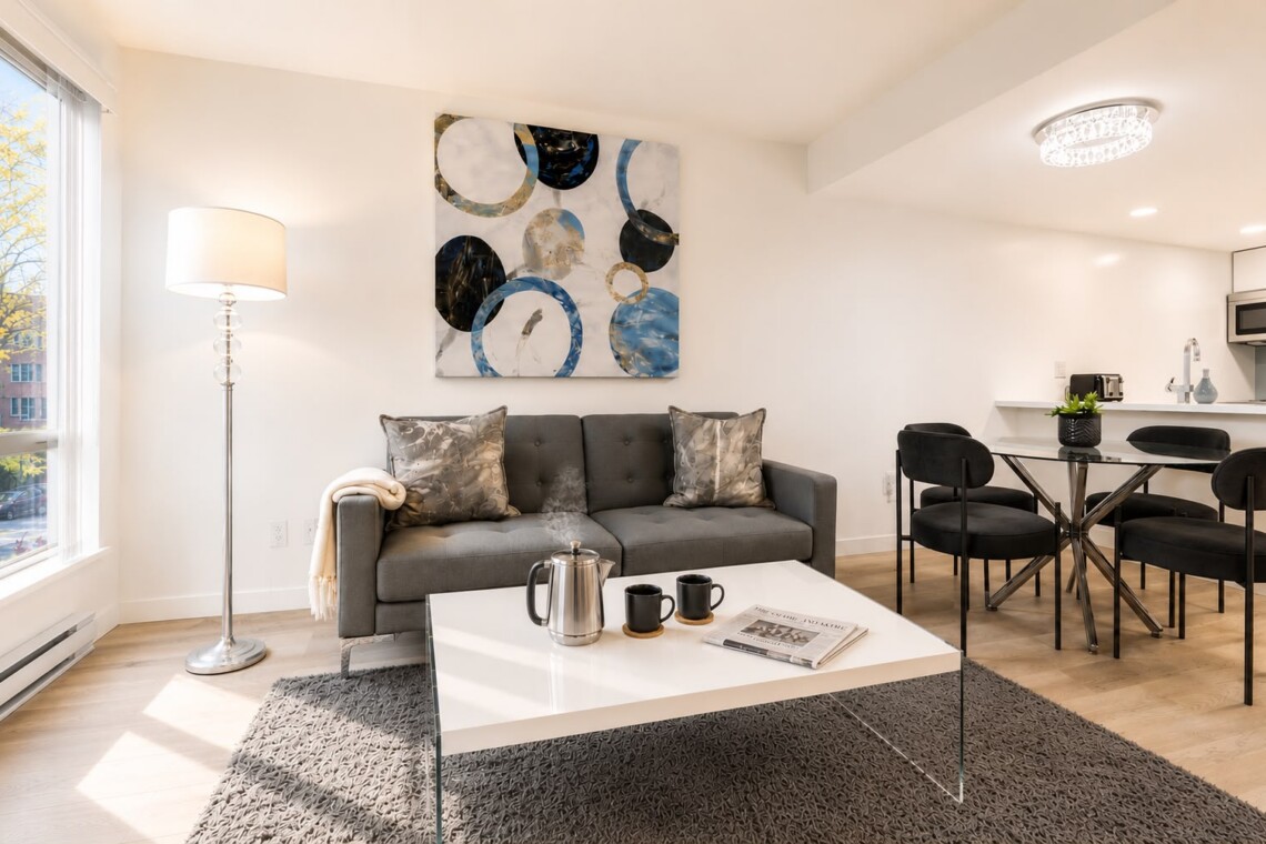 Bright, modern living room with gray sofa, abstract art, and glass coffee table in front of a large window