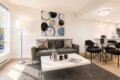 Bright, modern living room with gray sofa, abstract art, and glass coffee table in front of a large window