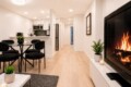 Open-concept living space with a lit fireplace on the right, glass dining table, black chairs, and a modern kitchenette in the background.