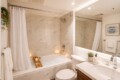 Modern bathroom with marble-tiled bath area, white shower curtain, and wood bath tray holding candles and small plant.