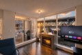 Modern living room with a lit fireplace, flat-screen TV, and floor-to-ceiling windows showing a sunset over a bridge and marina.