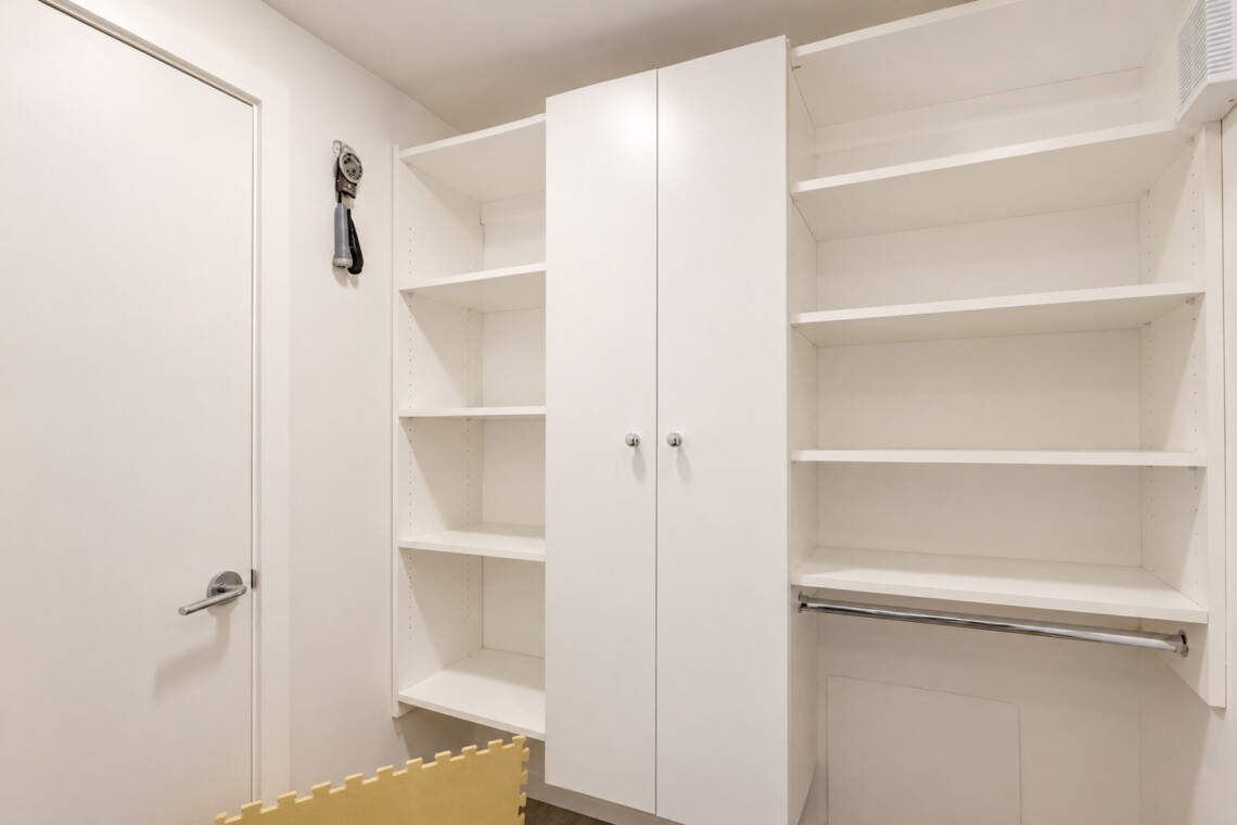 Corner of a white storage room with built-in shelves, a double-door cabinet, and a metal clothing rod beneath open shelves on the right side.