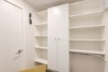 Corner of a white storage room with built-in shelves, a double-door cabinet, and a metal clothing rod beneath open shelves on the right side.