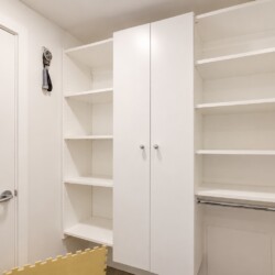 Corner of a white storage room with built-in shelves, a double-door cabinet, and a metal clothing rod beneath open shelves on the right side.