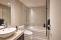 Contemporary bathroom with a glass shower enclosure, white bathtub, and a rounded white basin atop a beige countertop.