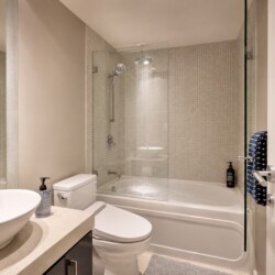 Contemporary bathroom with a glass shower enclosure, white bathtub, and a rounded white basin atop a beige countertop.