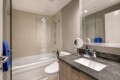 Modern bathroom with a glass-enclosed bathtub shower, beige wall tiles, and a dark marble countertop vanity.