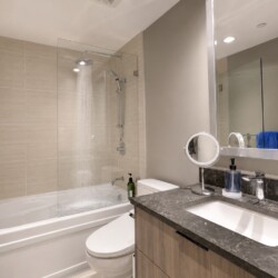 Modern bathroom with a glass-enclosed bathtub shower, beige wall tiles, and a dark marble countertop vanity.