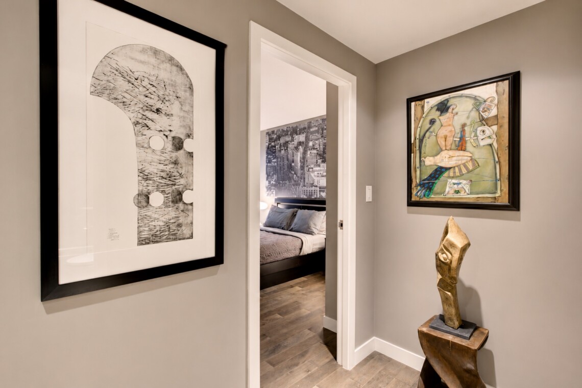 Hallway with two framed artworks and a wood sculpture beside an open doorway to a bedroom.