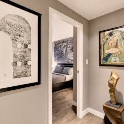 Hallway with two framed artworks and a wood sculpture beside an open doorway to a bedroom.
