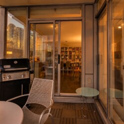 Sunset-lit balcony with a Weber grill, metal chair, and glass doors opening to a book-filled living room.