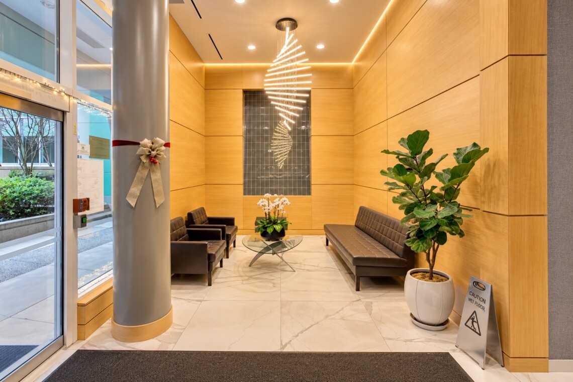Modern hotel lobby with wood paneled walls, leather seating, and a glass coffee table beneath a spiral chandelier.