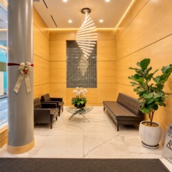 Modern hotel lobby with wood paneled walls, leather seating, and a glass coffee table beneath a spiral chandelier.