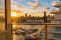 Sunset view over a marina with moored boats and a city skyline, seen from a balcony railing.