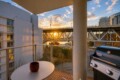 Balcony scene with a round table and red mug, a Weber grill on the right, and a sunset over a bridge and marina in the distance.
