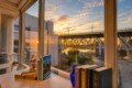Sunset view through a large window of a bridge over a harbor, with a desk in the foreground holding books and a blue vase.