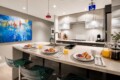 Modern kitchen with an island set for three: plates with croissants and berries, orange juice, and coffee mugs.