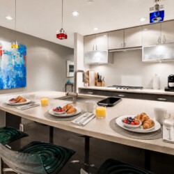 Modern kitchen with an island set for three: plates with croissants and berries, orange juice, and coffee mugs.
