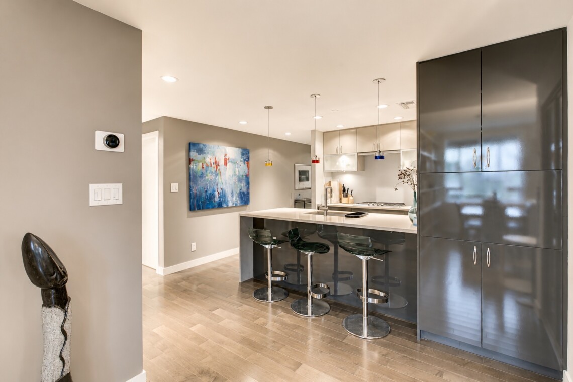 Modern open kitchen with a gray island, black bar stools, and tall glossy cabinets in a contemporary home.