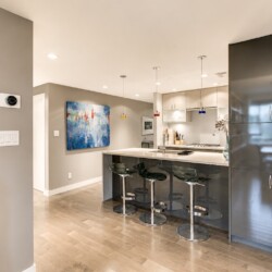 Modern open kitchen with a gray island, black bar stools, and tall glossy cabinets in a contemporary home.