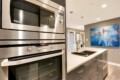 Modern kitchen with stainless steel built-in microwave and double ovens, gray cabinetry, and an island with a sink.