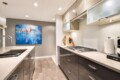 Modern L-shaped kitchen with gray lower cabinets, white countertops, and a gas cooktop under frosted glass cabinets; abstract blue painting on gray wall