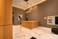Modern hotel reception area with a wood-fronted desk, white marble floor, gray textured walls, and warm LED trim lighting.