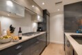 Modern L-shaped kitchen with gray lower cabinets, beige countertops, and a gas range; bowls of salad and bread with a wine bottle on the counter.