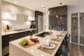 Modern kitchen with a long island, fruit board, wine bottle, and four place settings ready for dining at a breakfast bar.