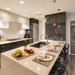 Modern kitchen with a long island, fruit board, wine bottle, and four place settings ready for dining at a breakfast bar.