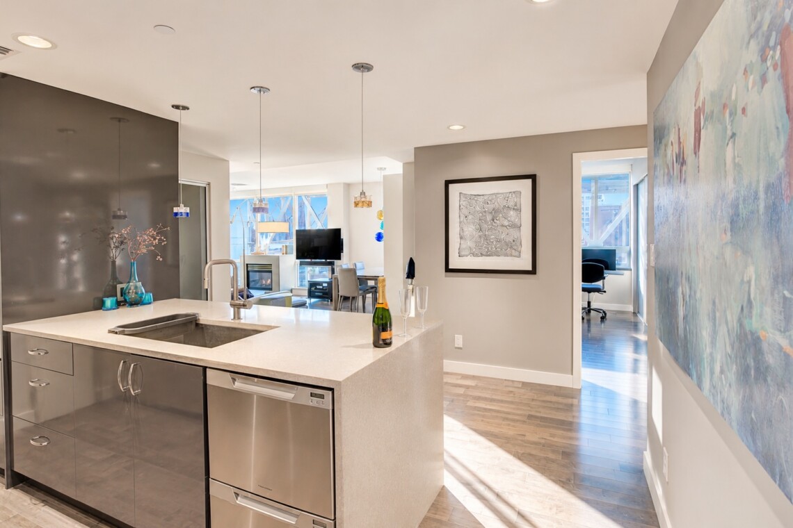 Open-concept kitchen with a white countertop island, sink, and stainless steel appliances; a champagne bottle and two flutes sit on the counter.