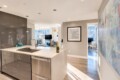 Open-concept kitchen with a white countertop island, sink, and stainless steel appliances; a champagne bottle and two flutes sit on the counter.