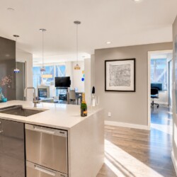 Open-concept kitchen with a white countertop island, sink, and stainless steel appliances; a champagne bottle and two flutes sit on the counter.