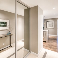 Modern hallway with a console table, framed artwork, and a blue vase with bare branches; sliding glass doors reflect the entryway.