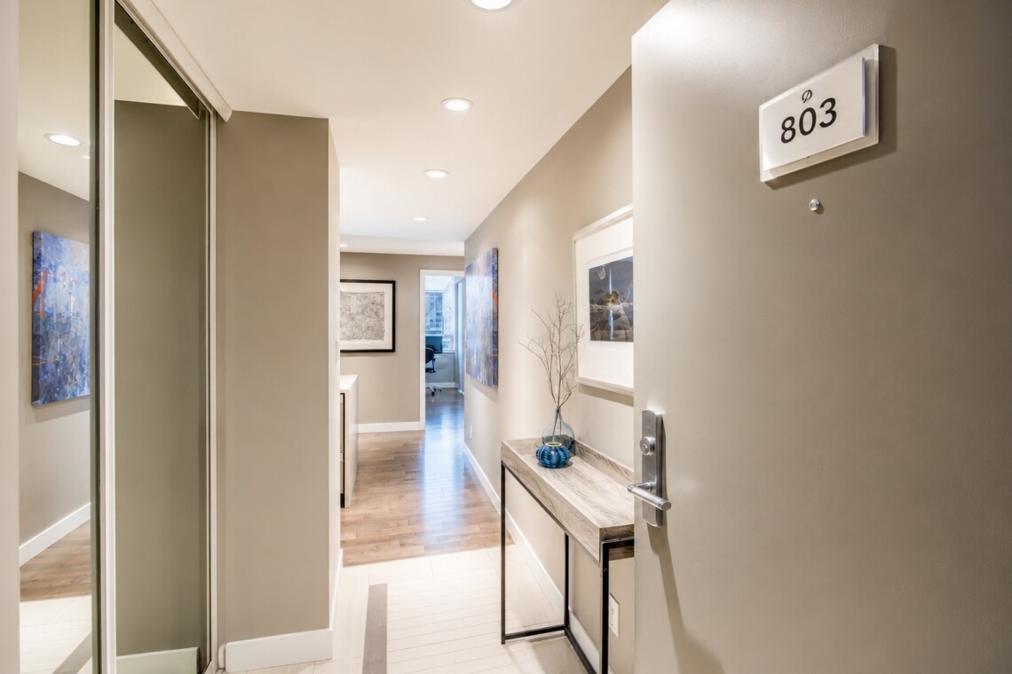 Entry hallway of a modern apartment with a console table, blue vase, and wall art leading to a lit interior room (803 door placard)