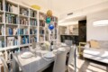 Open-concept living and dining space with a floor-to-ceiling white bookshelf wall, a glass dining table set for six, and colorful pendant lights above the table.