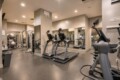 Row of treadmills in a modern gym with mirrors on the back wall and free weights to the left.