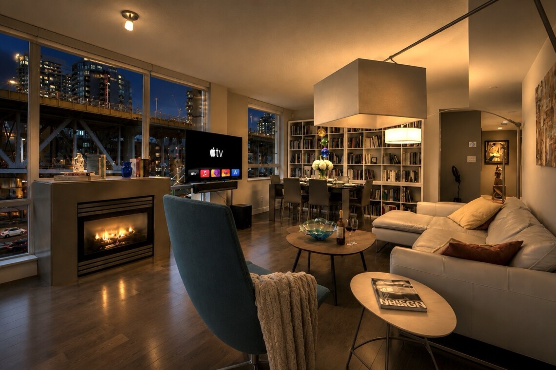 Cozy modern living room at night with a fireplace, large windows showing the city skyline, and a white sectional sofa.