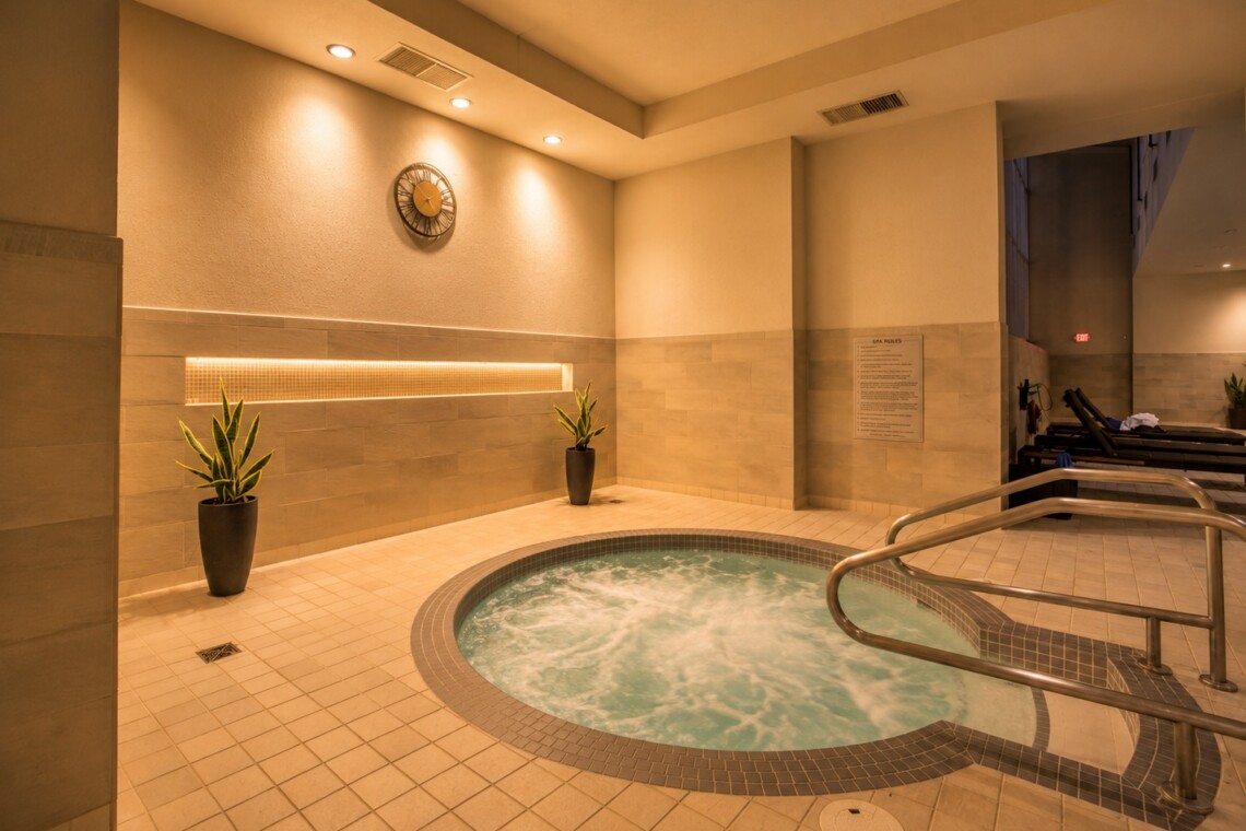 Indoor spa area with a circular bubbling hot tub, beige tiled floor, and soft overhead lighting.