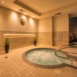 Indoor spa area with a circular bubbling hot tub, beige tiled floor, and soft overhead lighting.