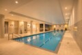 Indoor pool area with beige tile floors and walls, soft overhead lighting, and lounge chairs along the far wall; a calm blue rectangular pool in the center. Depth markers run along the pool edge.