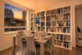 Sunset-lit dining room with a glass table set for six, a white bookshelf wall, and colorful hanging glass orbs by the ceiling window.