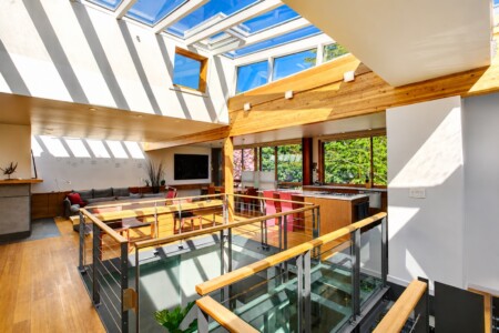 Bright open-plan living and kitchen area with skylight ceiling, wooden beams, and a glass-railed mezzanine.